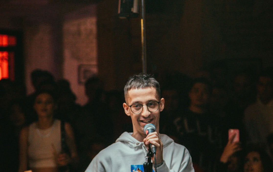 Young male singer performing live in a lively nightclub setting, engaging crowd.
